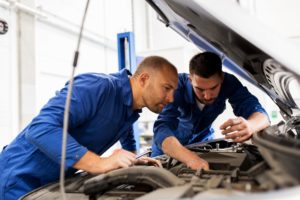 Kfz-Mechaniker kontrollieren den Motor eines Autos in der Werkstatt.