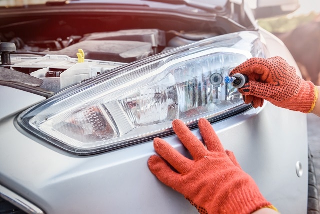 Mann hält eine Glühbirne hoch vor Scheinwerfer | autoreparaturen.de